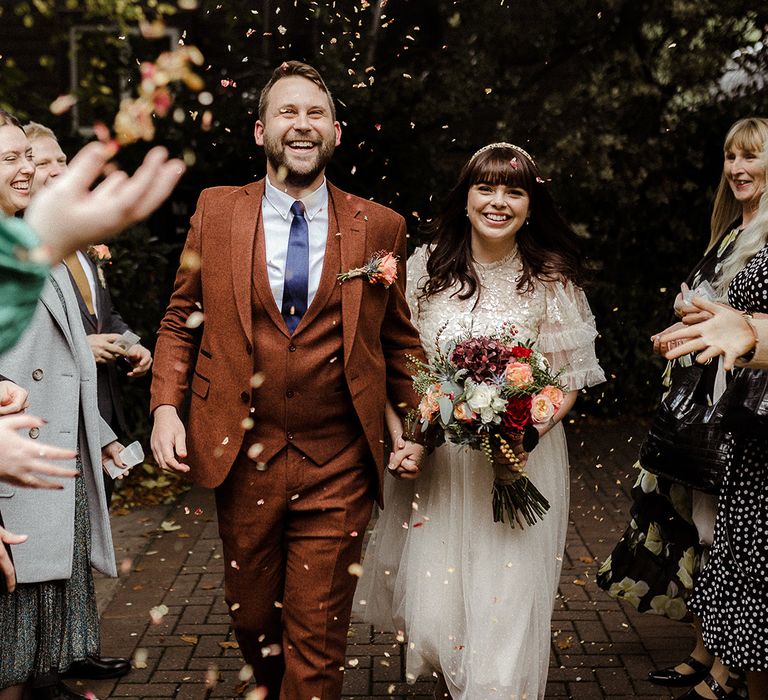 Bride and groom smile widely together as they exit their ceremony to confetti 