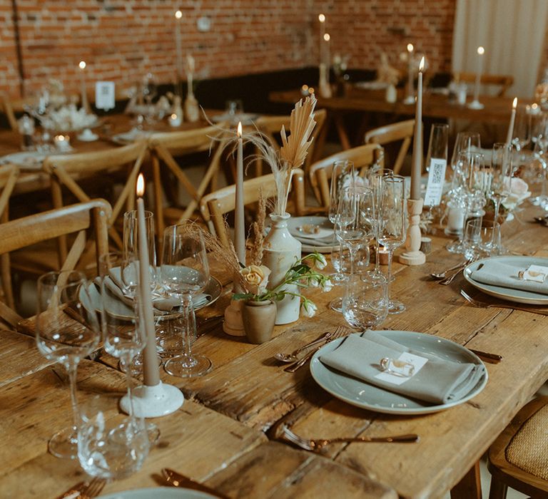 Wooden banquet table with grey tapered candles, plates and napkins and dried flowers