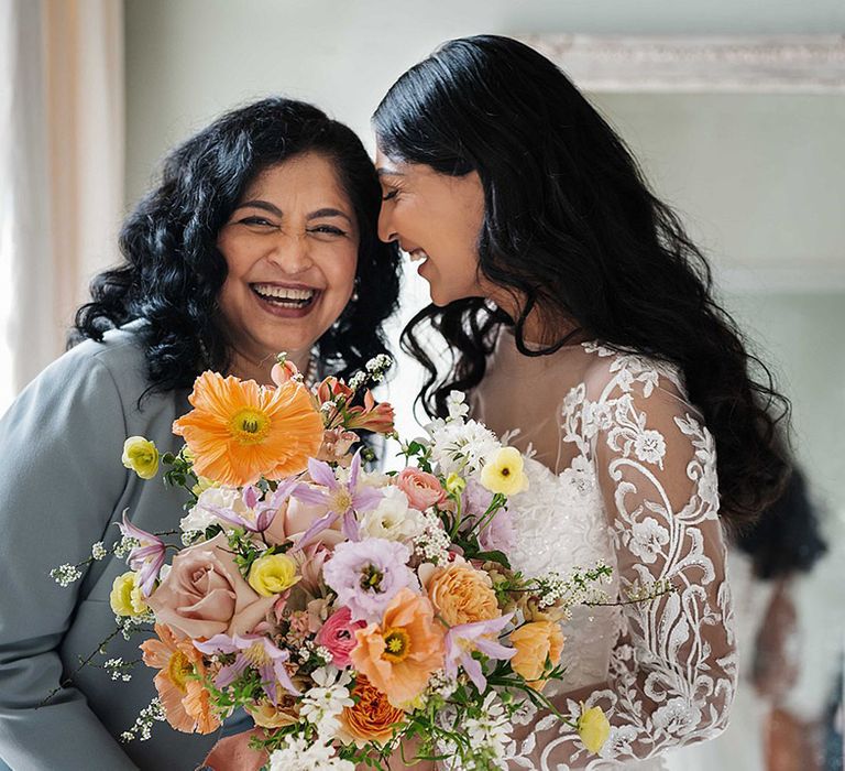 Bride in illusion lace long sleeve white wedding dress holds colourful spring bouquet with giant poppy and roses