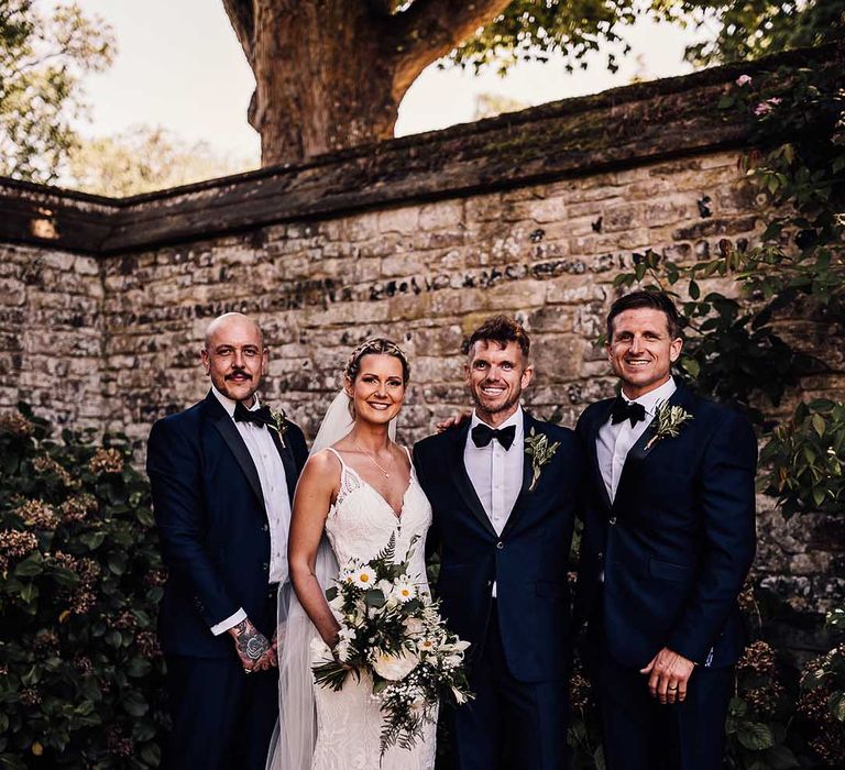 Bride in white lace wedding dress with white flower bouquet and groomsmen in matching blue tuxedo 