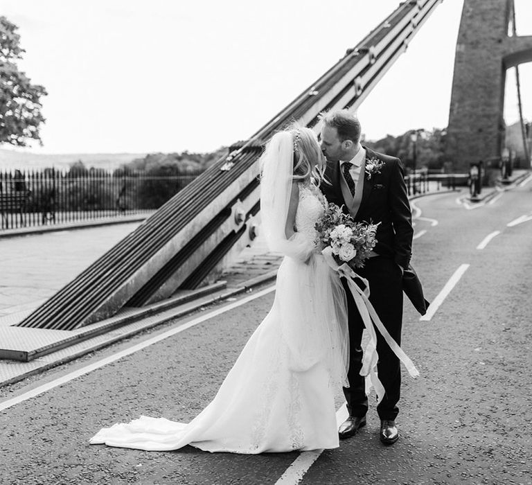 Bride and groom share a kiss standing on the Clifton suspension bridge in Bristol 