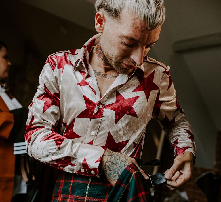 Groom wears white and red star shirt tucked into Tartan kilt on the day of his wedding 