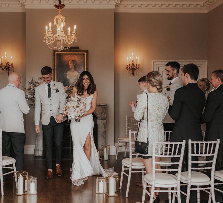 Bride and groom walk back down the aisle as a married couple at their romantic wedding with chandeliers and pillar candles 