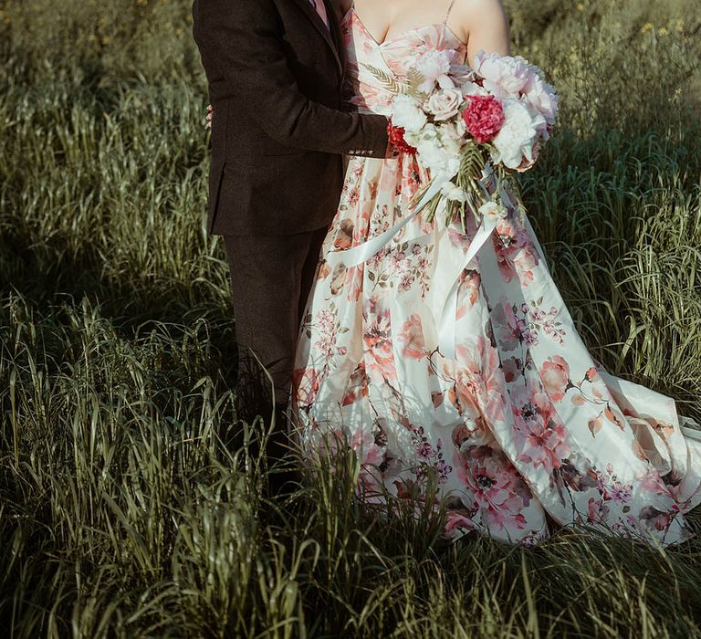 Bride in a pink flower hand painted silk wedding dress smiling with the groom in a brown suit and pink tie for botanical style wedding