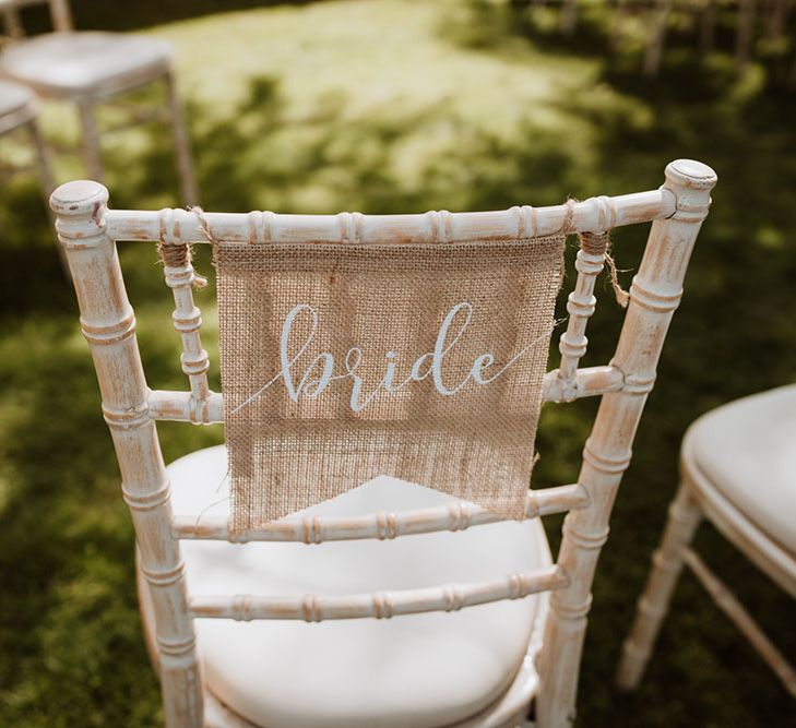 Hessian fabric tied to chair with bride written across in white writing 