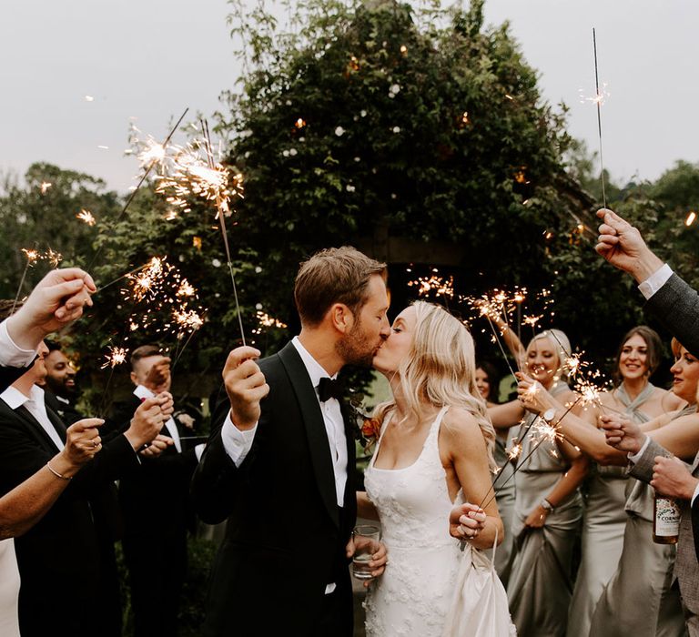 The wedding party waves sparklers for the bride and groom as they share a kiss 