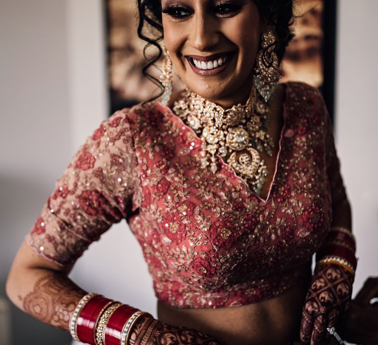 Indian bride wears beautifully embellished lehenga complete with bold jewellery and her black hair tied back in curls 