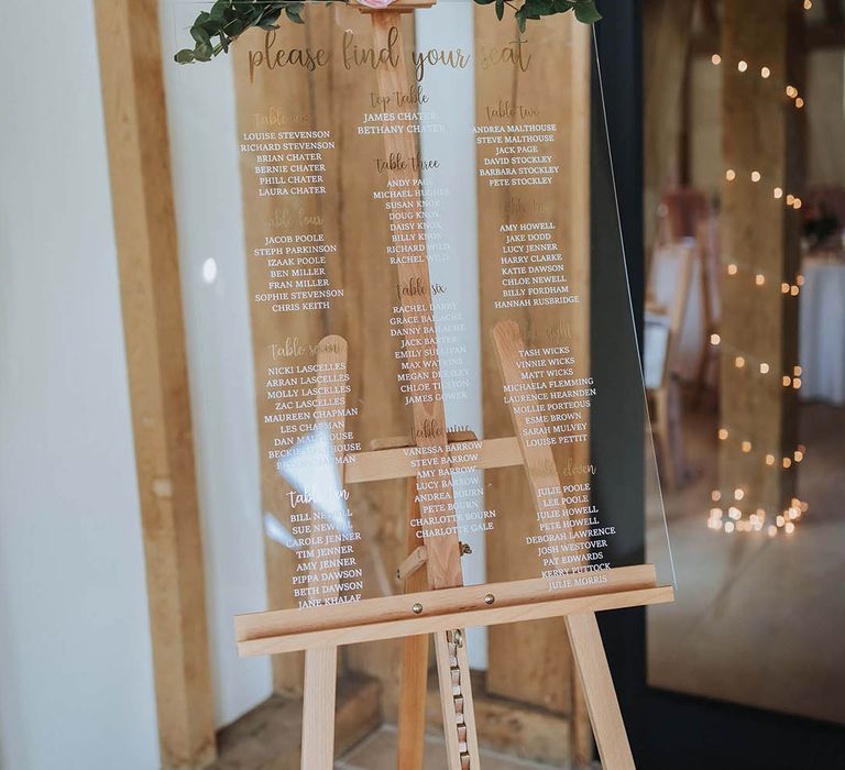 Clear acrylic wedding table plan on a wooden easel with pink flower and foliage decor 