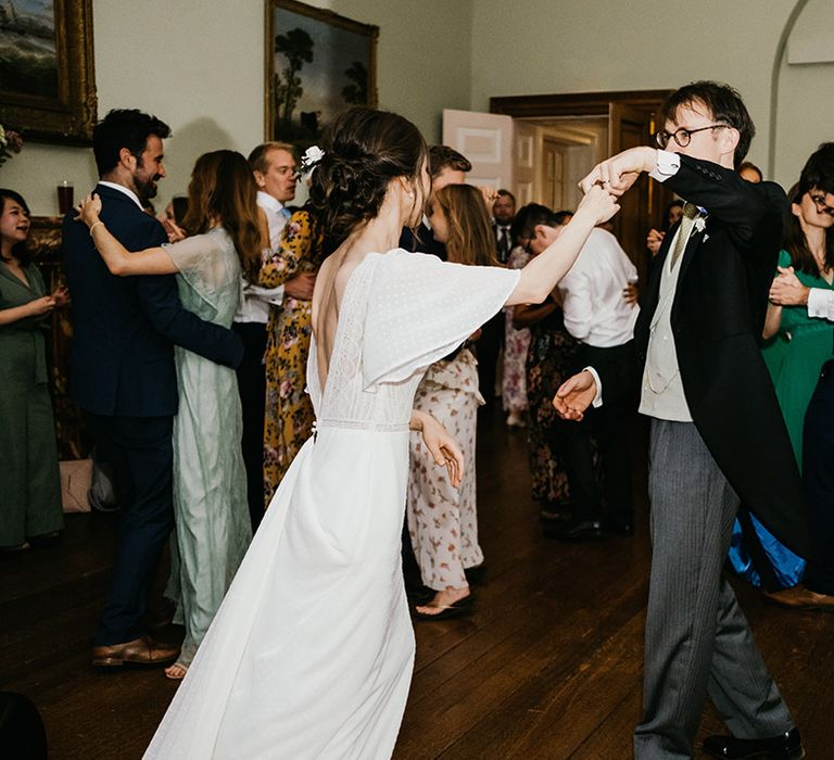 Bride in open back wedding dress with batwing sleeves and groom in three piece suit dancing at their wedding reception in Kelmarsh Hall