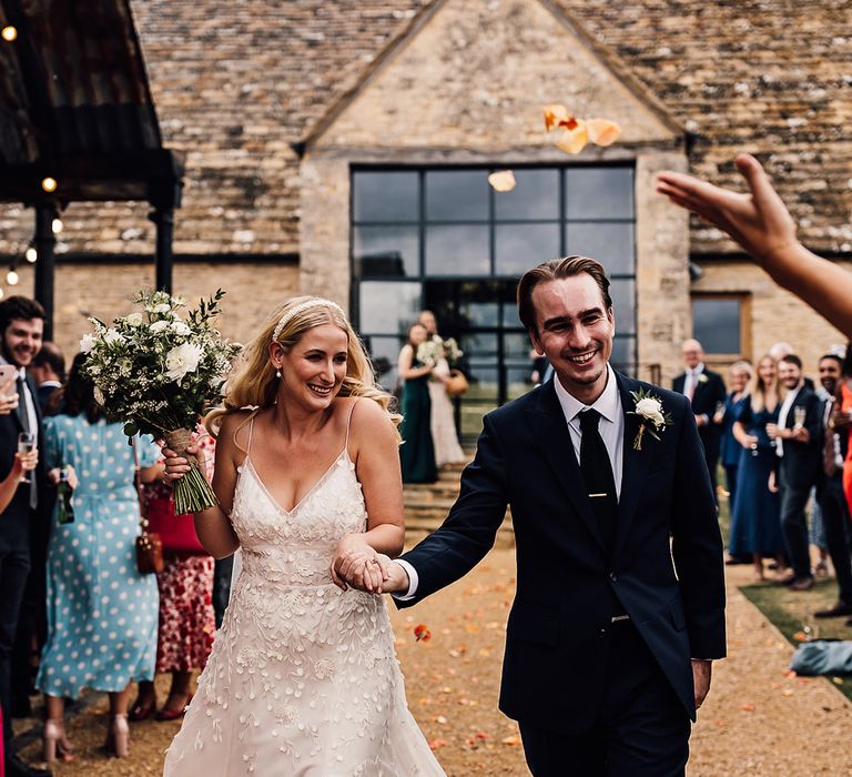 Bride in an Alexandra Grecco Lana dress having a confetti exit with the groom in a navy blue suit 