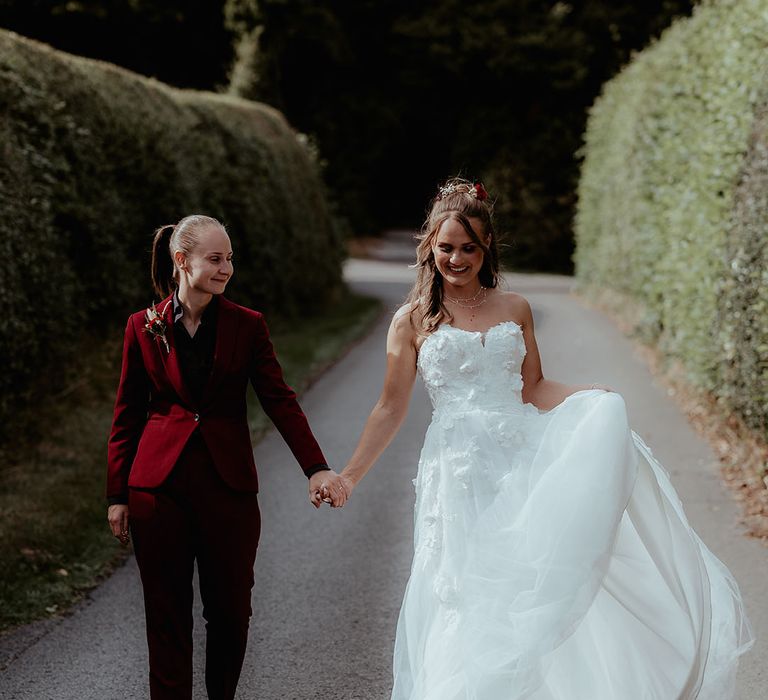 Bride with burgundy suit with black shirt walking with the bride in a strapless flower wedding dress