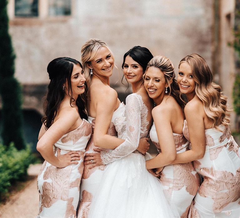 Smiling bridesmaids in white sweetheart strapless dresses with rose gold pattern smiling with the bride 