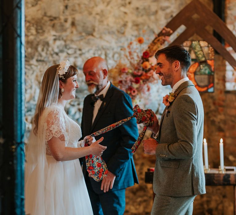 The bride and groom stand together at the altar for their hand fasting ceremony with a floral fabric 