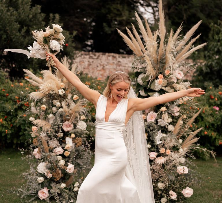 The bride poses in front of two tall flower columns with pampas grass 