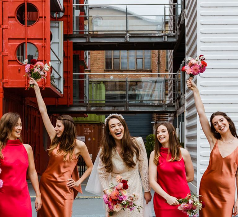 Bridesmaids in bright red and copper colour satin dresses with the bride in a lace Rixo wedding dress