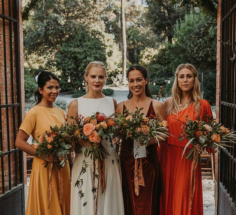 The bridesmaids in yellow, red, and orange bridesmaid dresses smiling for autumn wedding with the bride 