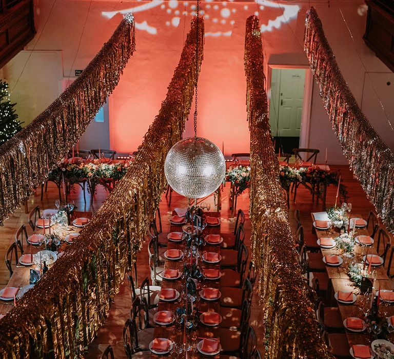 Gold wedding streamers, Christmas tree projection, large hanging disco ball and Christmas-themed wedding tablescapes in reception room of London wedding venue 