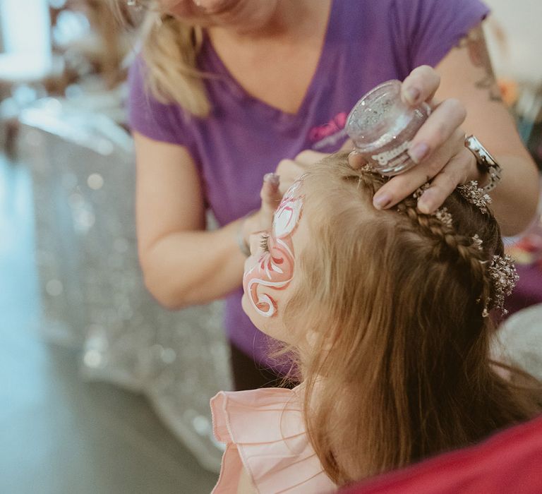 Young girl gets her face painted for the kids entertainment at the bouncy castle wedding in autumn 