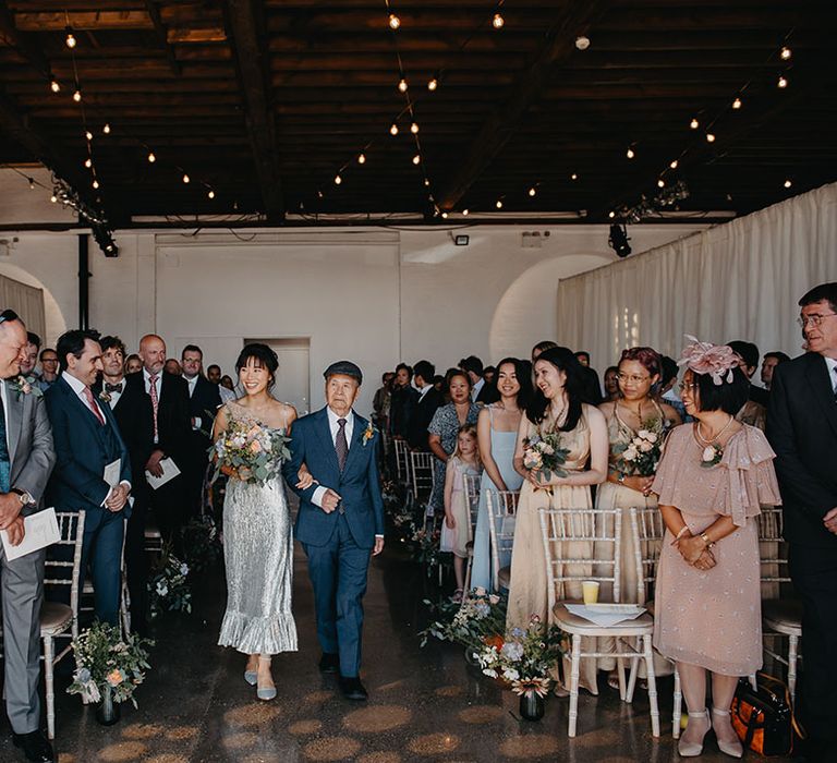 Bride in silver wedding dress walks down the aisle with her father at Trinity Buoy Wharf