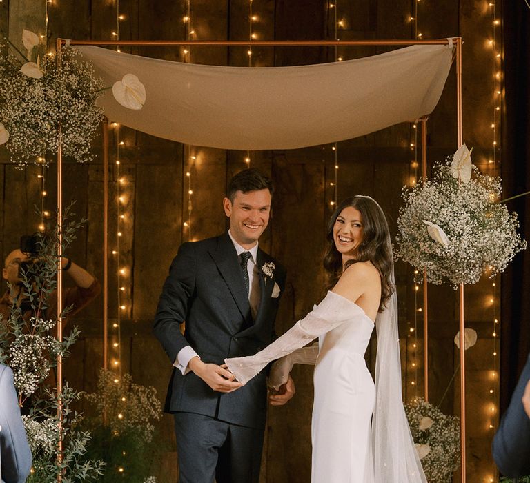 The bride and groom standing at the altar for their bespoke interfaith blessing ceremony with Jewish traditions with gypsophila and anthuriums 