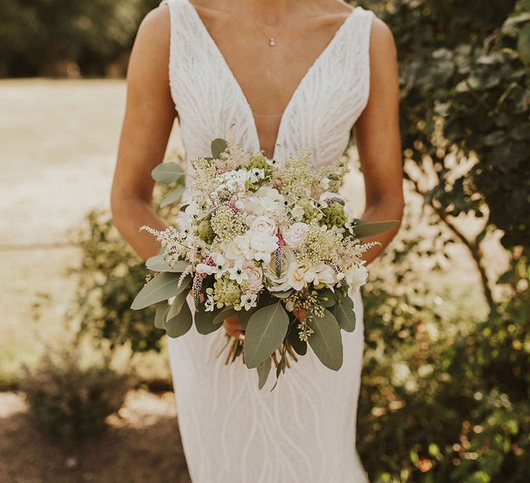 Bride in a beaded wedding dress holding a white and pink flower wedding bouquet with foliage 