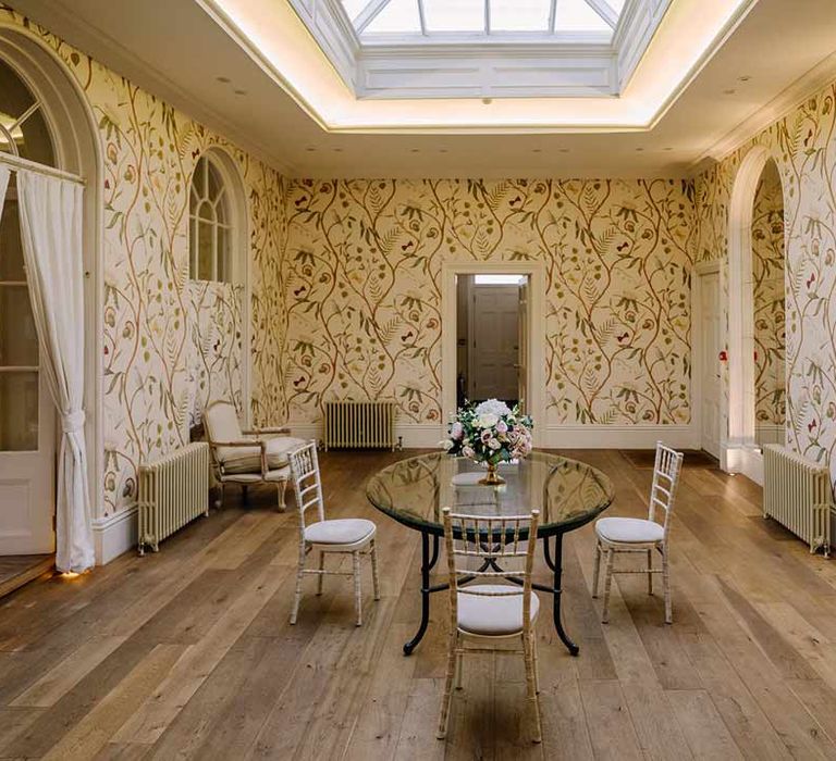 One of the rooms in Braxted Park wedding venue with light yellow floral wallpaper and luxe cream and gold furniture 