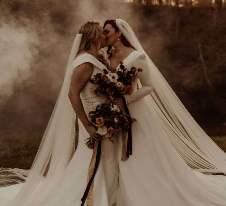 Bride in satin short sleeve deep v wedding dress and church length veil and bride in long sleeve deep v wedding dress and church length veil doing couples photoshoot at Hidden River Cabins