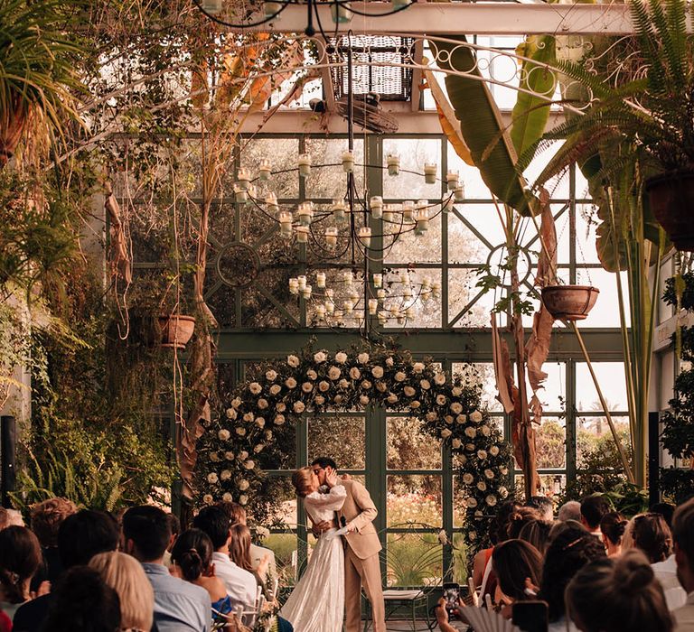 Bride and groom share romantic first kiss as a married couple in front of the white rose floral arch altar decor 