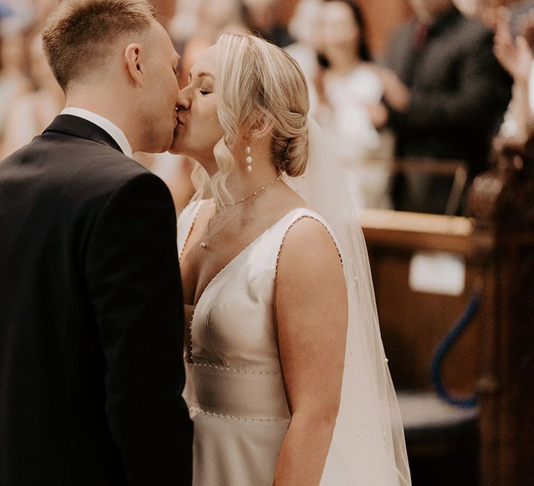 The bride and groom share their first kiss as a married couple at their church wedding 