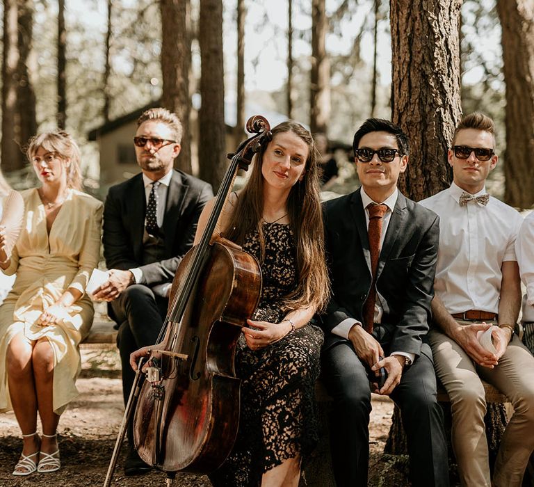 Wedding guests and wedding musician sit together to watch the woodland humanist ceremony 