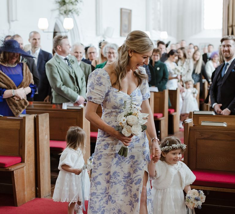 Flower girls in white dresses walk down the aisle with bridesmaids at church wedding 