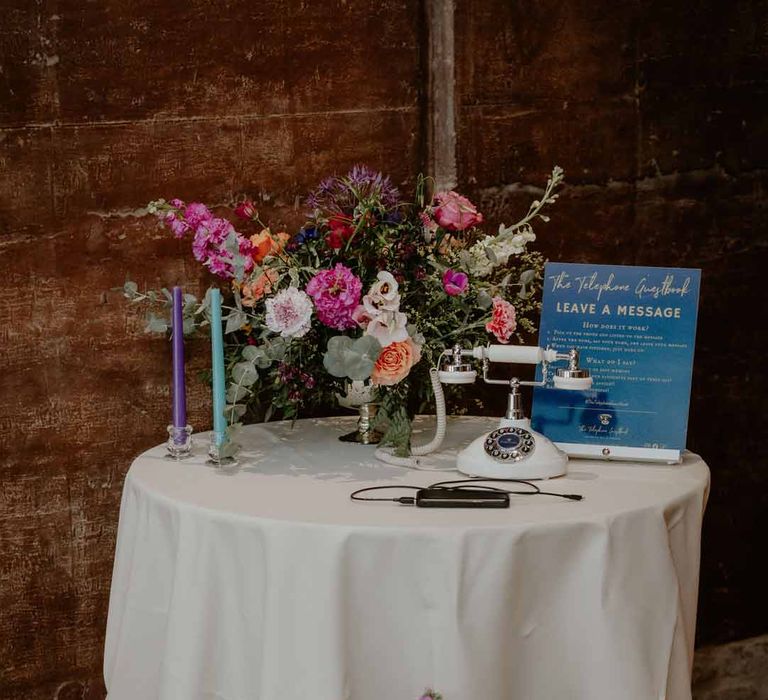 Round table with spring flower arrangements and rotary phone wedding guestbook with purple and teal tapered candles at Elmore Court Gloucestershire 