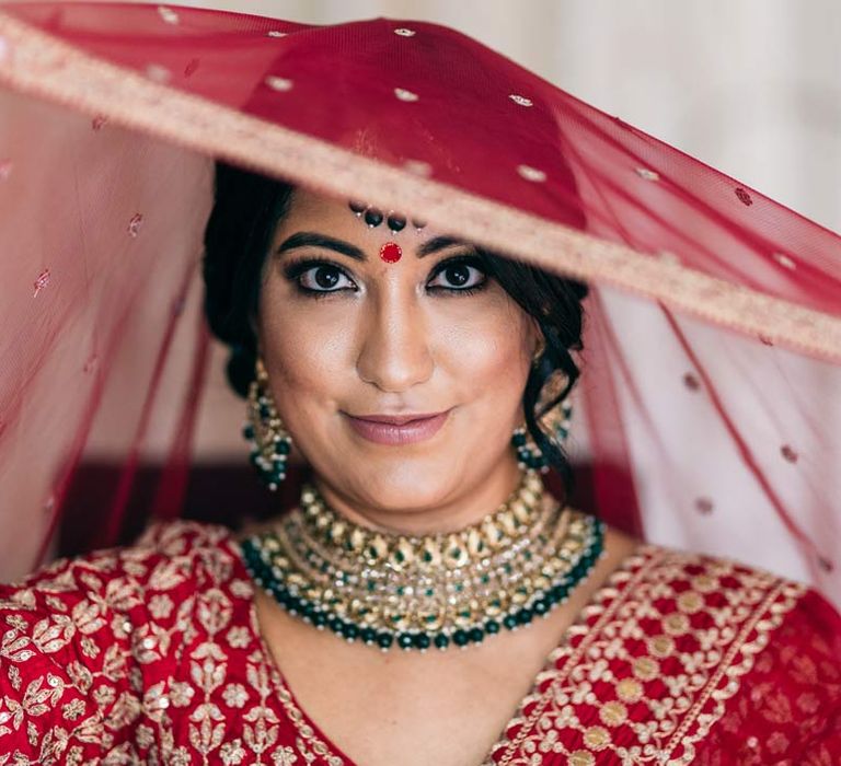 Bride in red and gold lehenga and gold and forest green bridal jewellery 