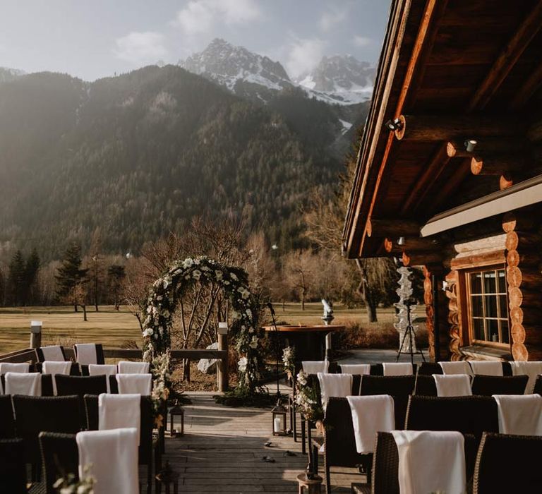 White garden rose, eucalyptus, baby's-breath and foliage wedding flower arch at outdoor wedding ceremony space at La Cabana Des Praz French destination ski wedding with the French alps in the background