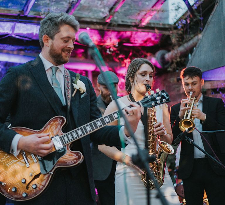 The groom plays a guitar while the bride plays a saxophone with his band for the wedding entertainment during the reception 