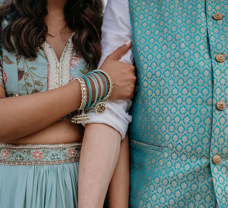 Bride and groom in traditional turqouise and pink floral South Asian wedding outfits with bangle bridal accessories