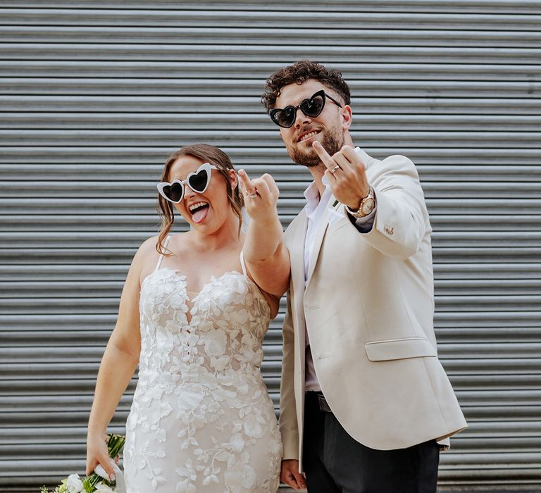 The bride and groom wearing black matching sunglasses show off their wedding ring finger with their new wedding bands 