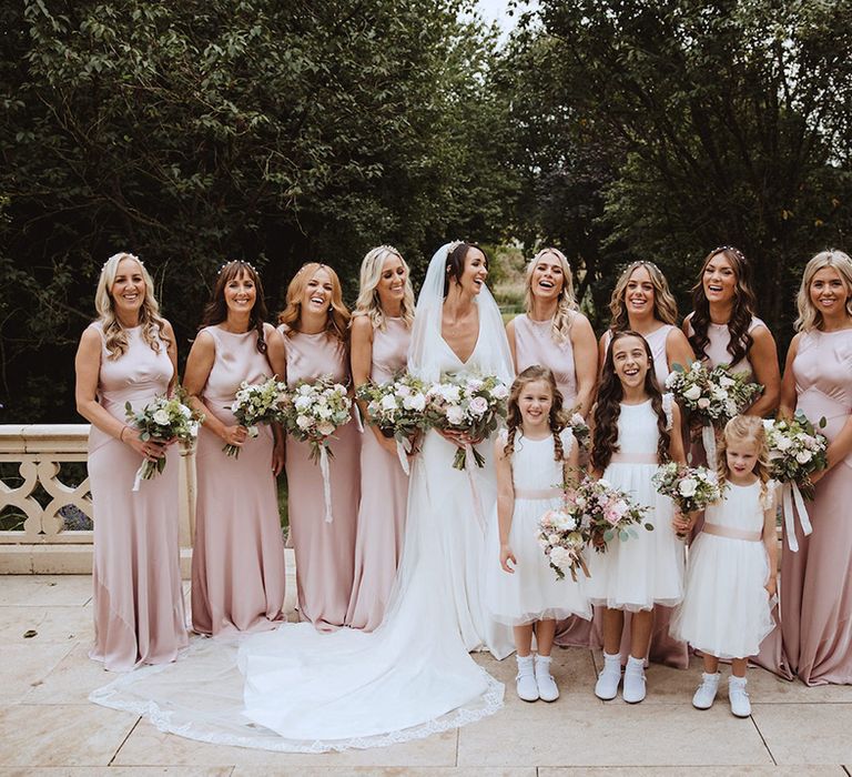 Bridal party wearing blush pink bridesmaid dresses with flower girls in white dresses 