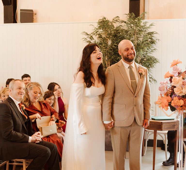 Groom wearing light beige checkered suit with the bride in a bespoke wedding dress at their civil ceremony 