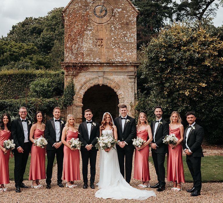 Group wedding party photo with the groomsmen in black tie and the bridesmaids in pink coral bridesmaid dresses