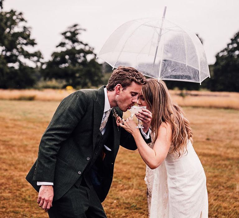 Bride and groom drinking wedding cocktails in the rain under an umbrella 