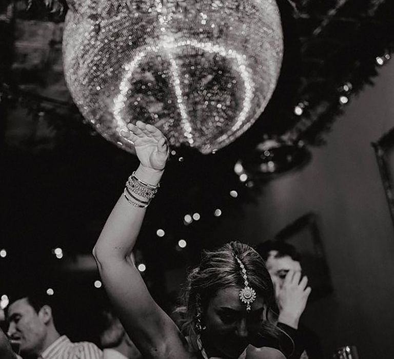 Black and white image of bride dancing under a disco ball at her wedding reception by Bowl Of Corks Photography