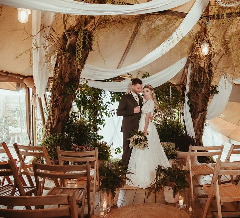 The Garden Tipi no waste wedding with drapery and sustainably sourced wedding fashion with brie in floral wedding dress and groom in brown wedding suit 