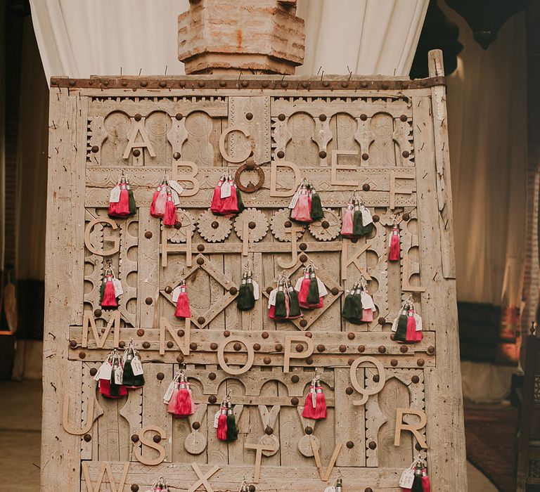 Escort cards seating chart with tassels and luggage tags hooked to the alphabet. 