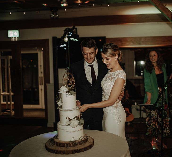 Bride and groom cutting their three tier wedding cake on rustic cake stand