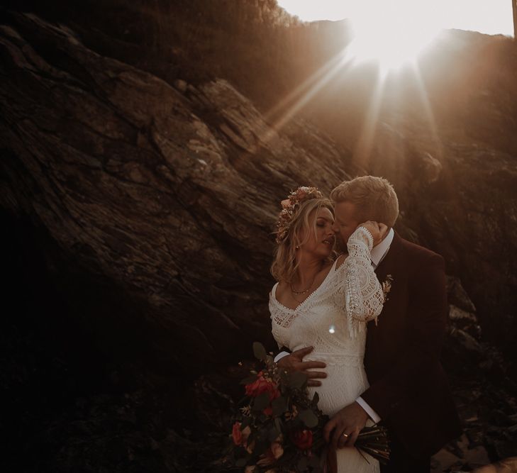 Bride and groom pose together at golden hour with a flower crown and large autumnal bouquet