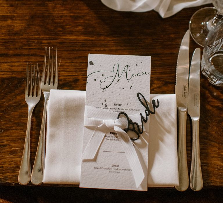 Emerald green and white wedding menu placed on white napkin and plate with Robert welch cutlery and eucalyptus decoration 