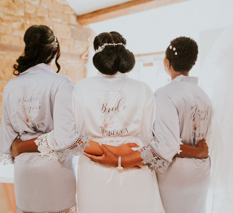 A bride stands with hr two bridesmaids. They have their backs to the camera and have their arms around each other. They show great examples of hairstyle for Black brides.