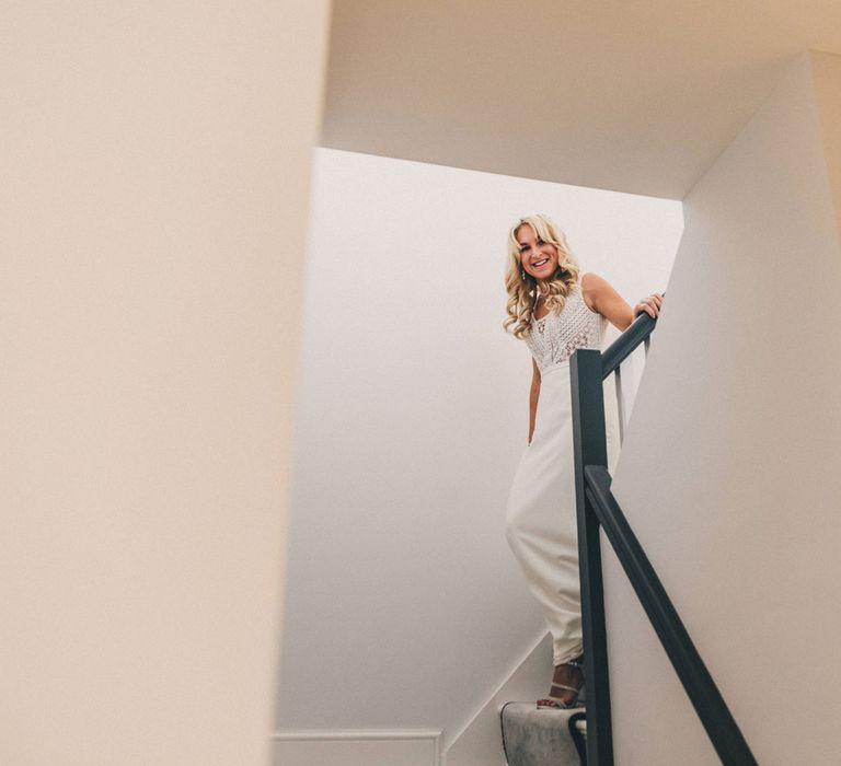 Smiling bride walking downstairs in Justin Alexander wedding dress for first look