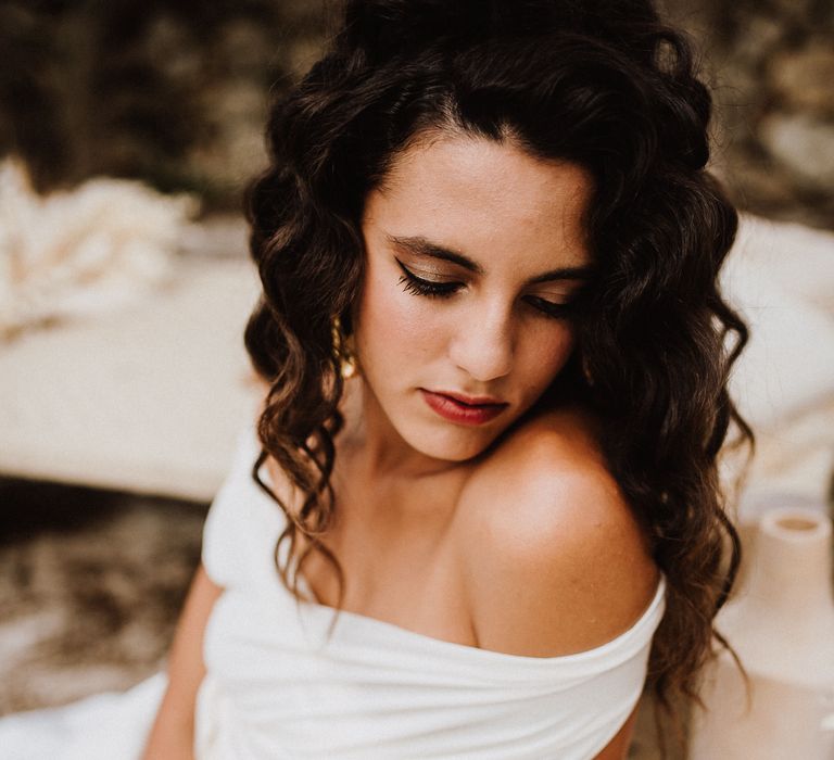 Boho bride wearing white off the shoulder gown with dark crimped hairstyle